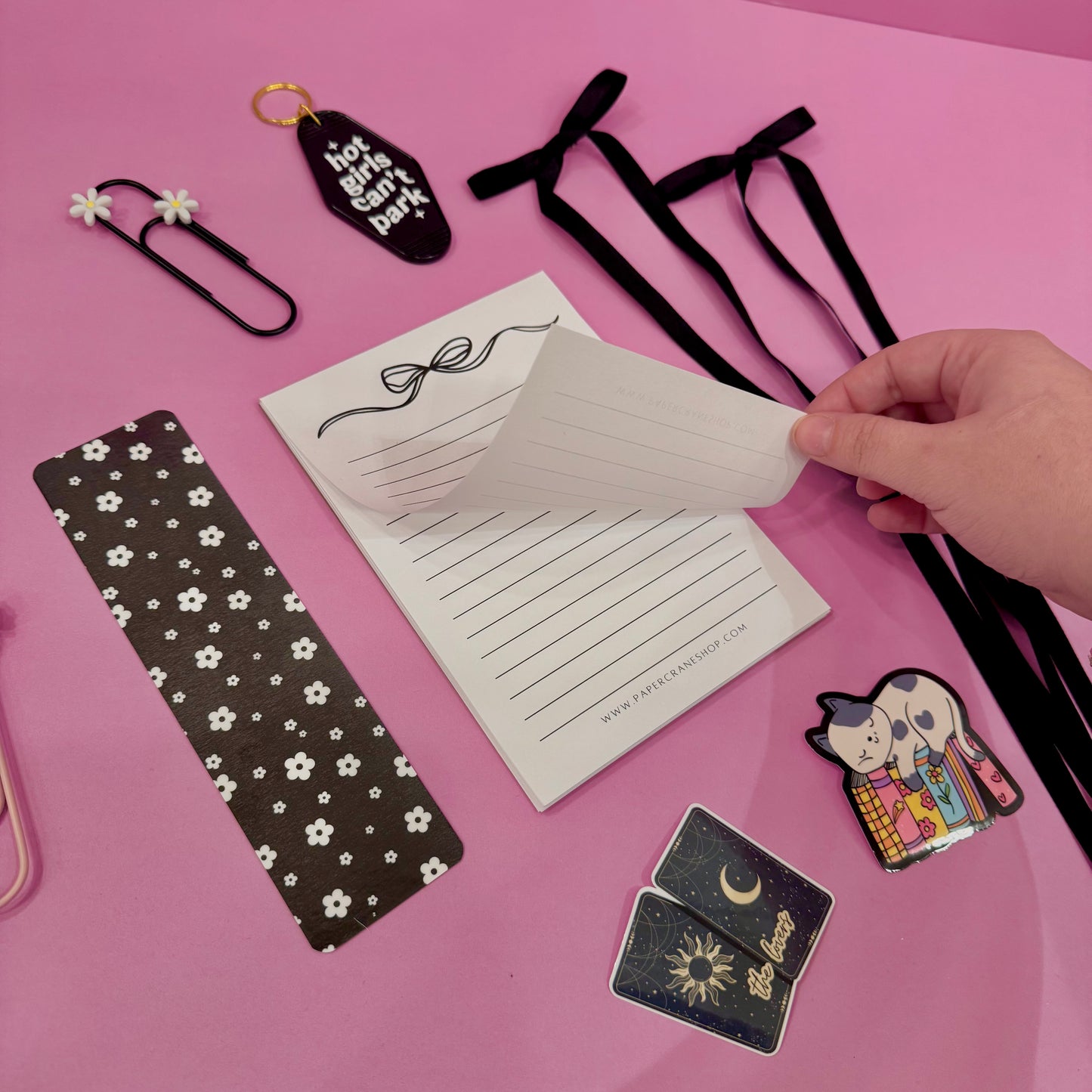 Stationery items including a bookmark, cards, and decorative ribbons on a pink background