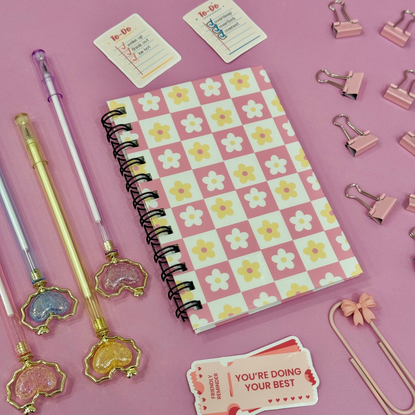 Floral notebook with decorative pens and clips on a pink background