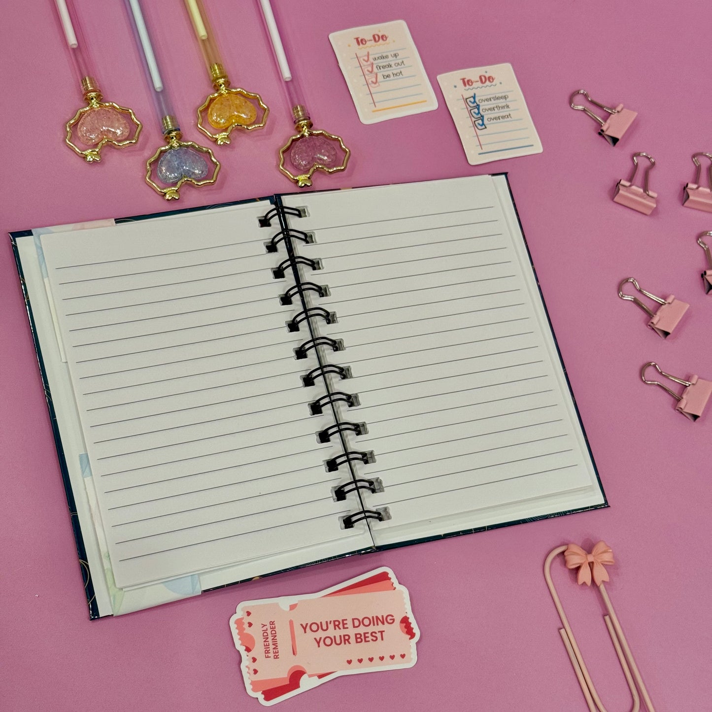 Open notebook with stationery items on a pink background