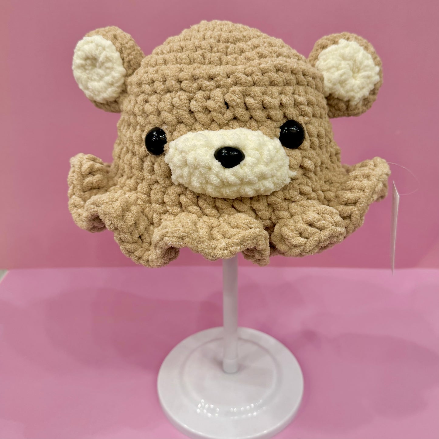 Crocheted bear hat on a mannequin head against a pink background