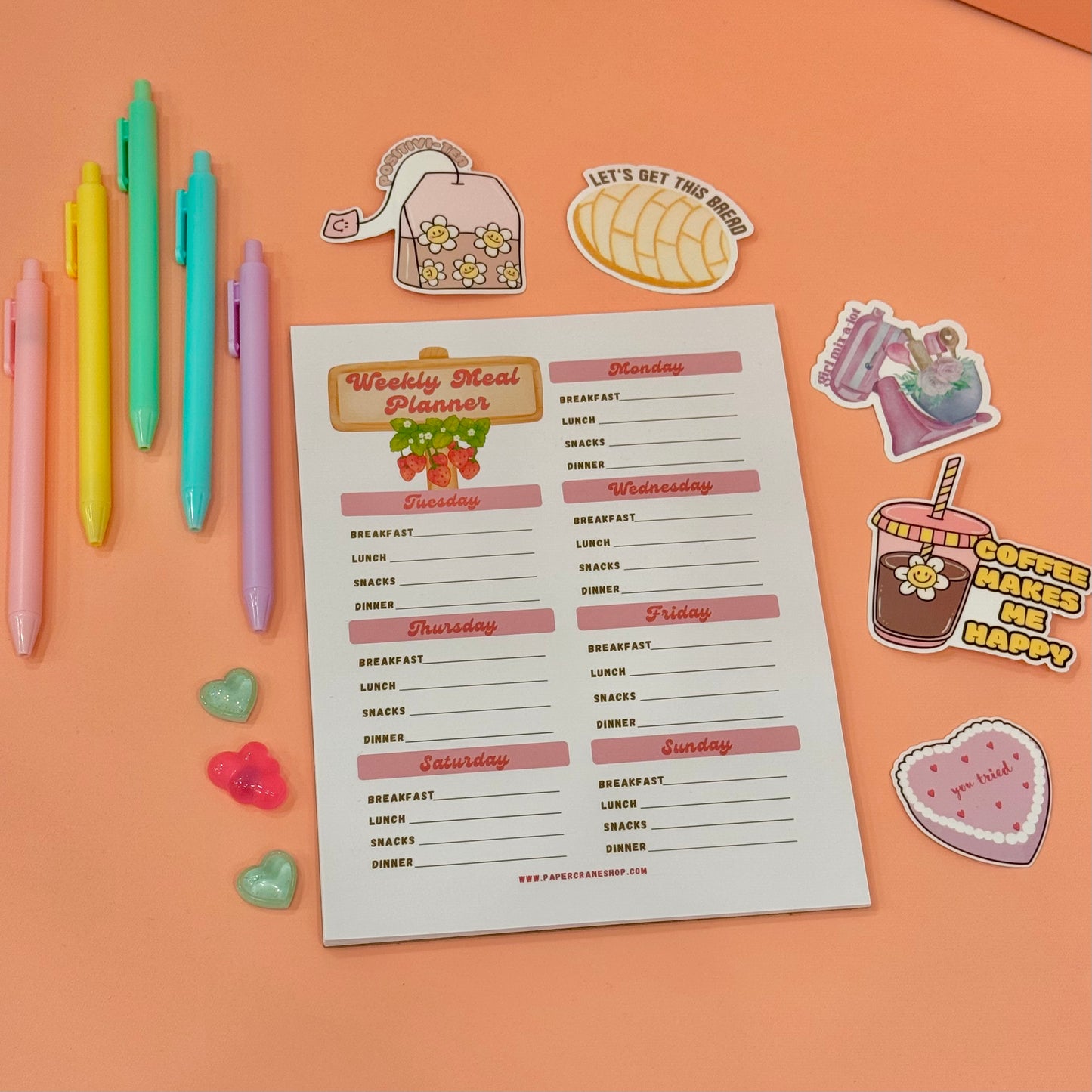 Weekly meal planner sheet with colorful pens and stickers on an orange background