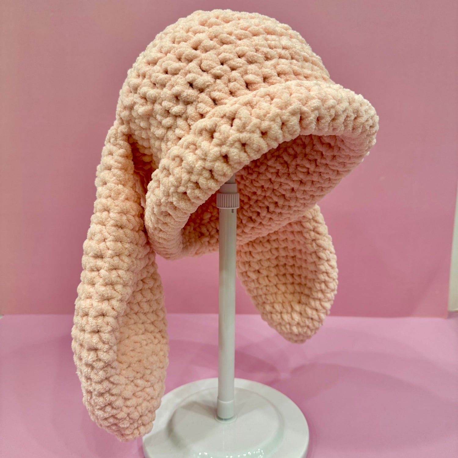 Knitted bunny hat with earflaps on a mannequin head against a pink background