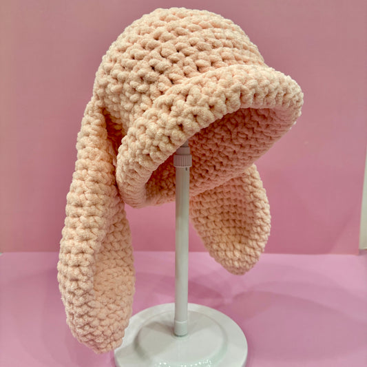 Knitted bunny hat with earflaps on a mannequin head against a pink background