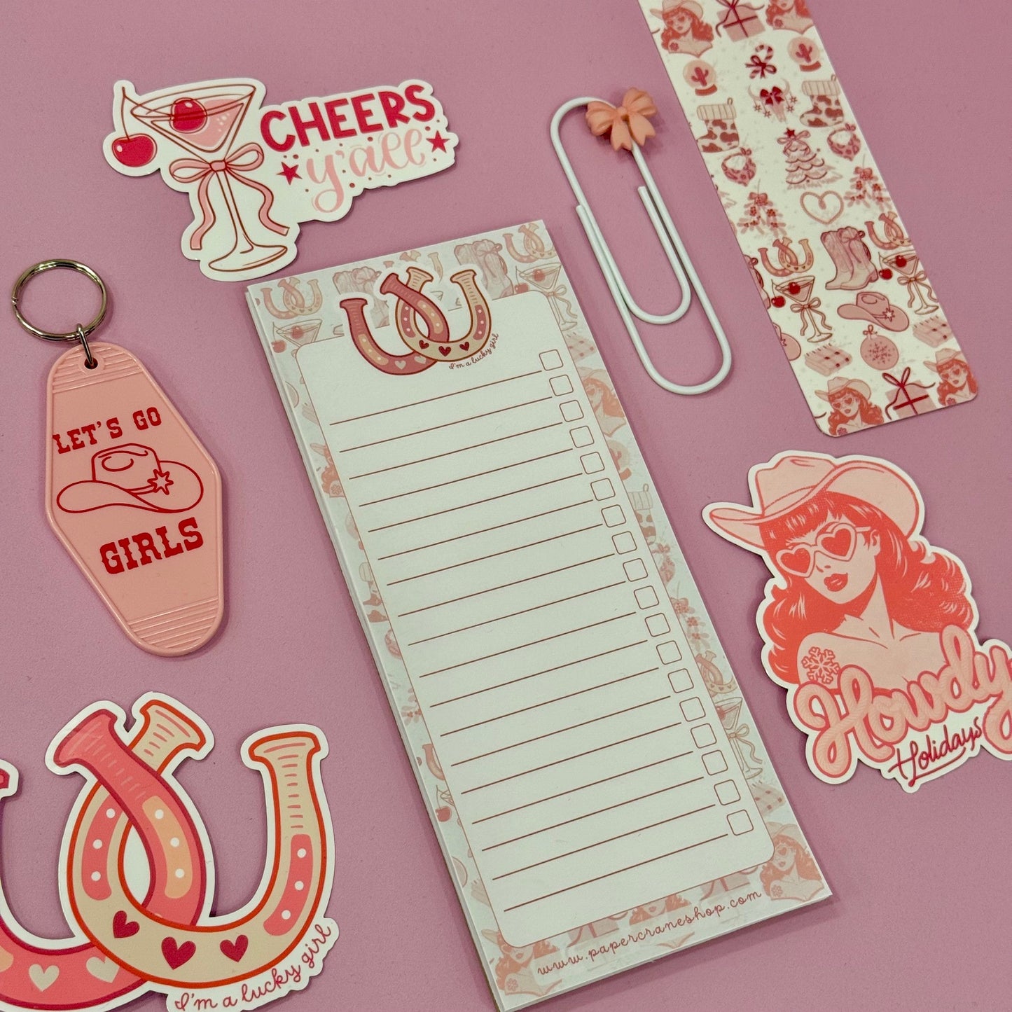 Collection of decorative items including a keychain, paper clips, and stickers on a pink background.
