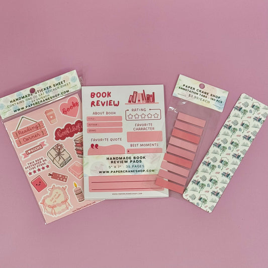 Collection of stationery items including a book review sheet, stickers, and a bookmark on a pink background.
