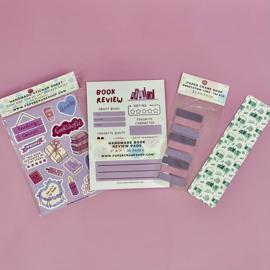 Collection of stationery items including stickers, a book review sheet, and a bookmark on a pink background.