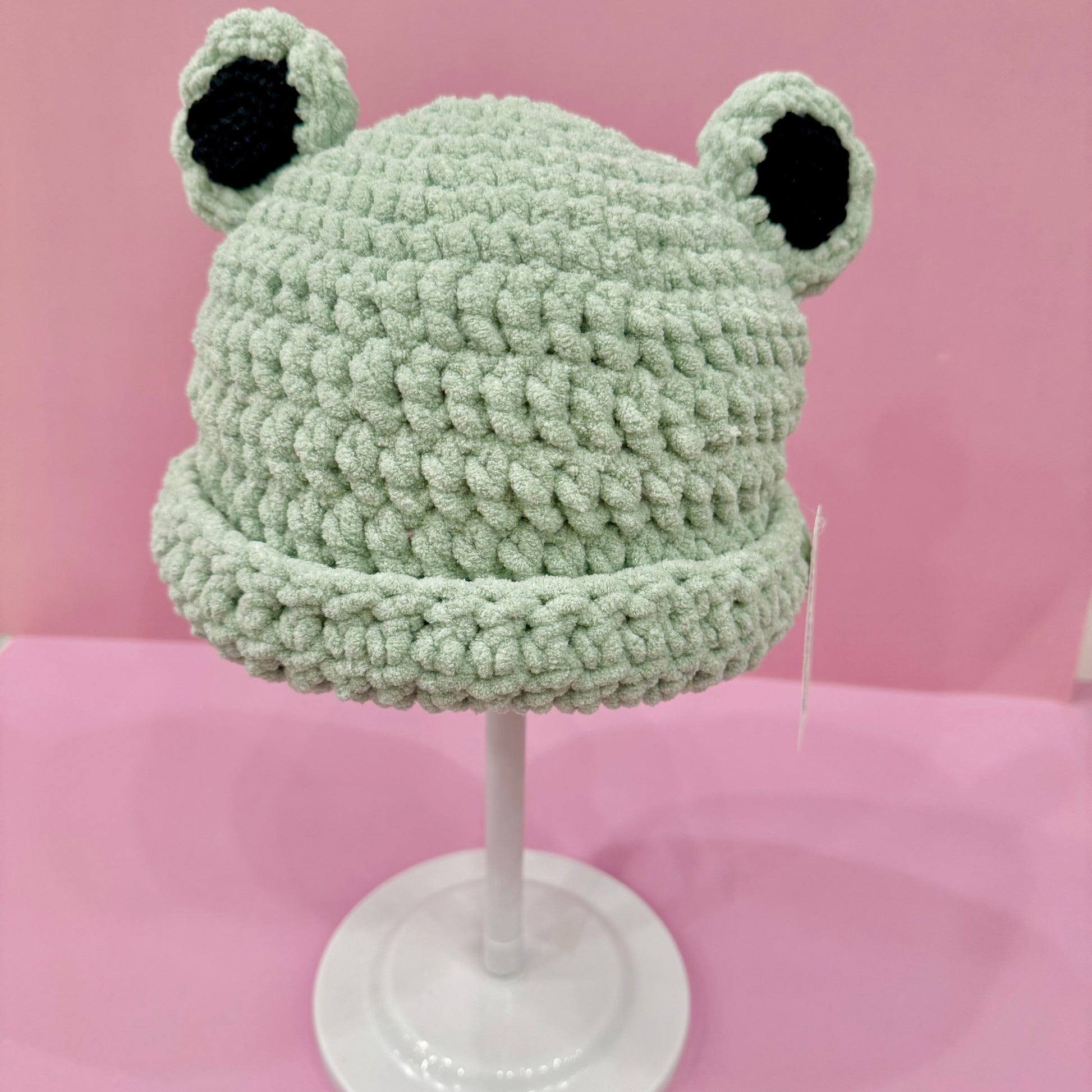 Green frog-shaped knitted hat on a pink background