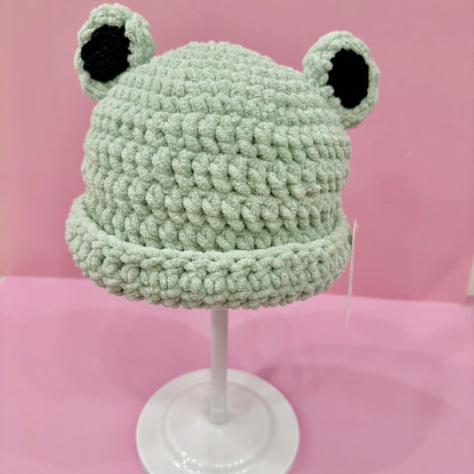 Green frog-shaped knitted hat on a pink background