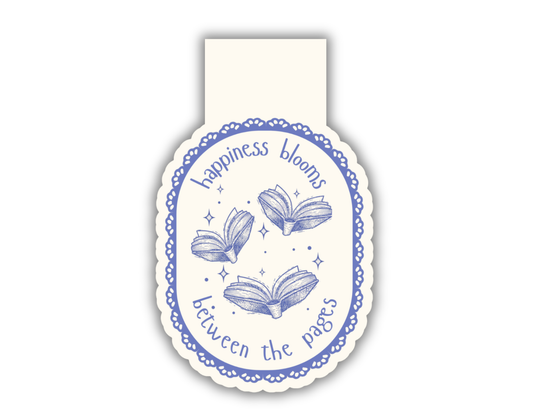 A magnetic bookmark with a cream background and blue decorative border, featuring three open books and the text 'happiness blooms between the pages'.