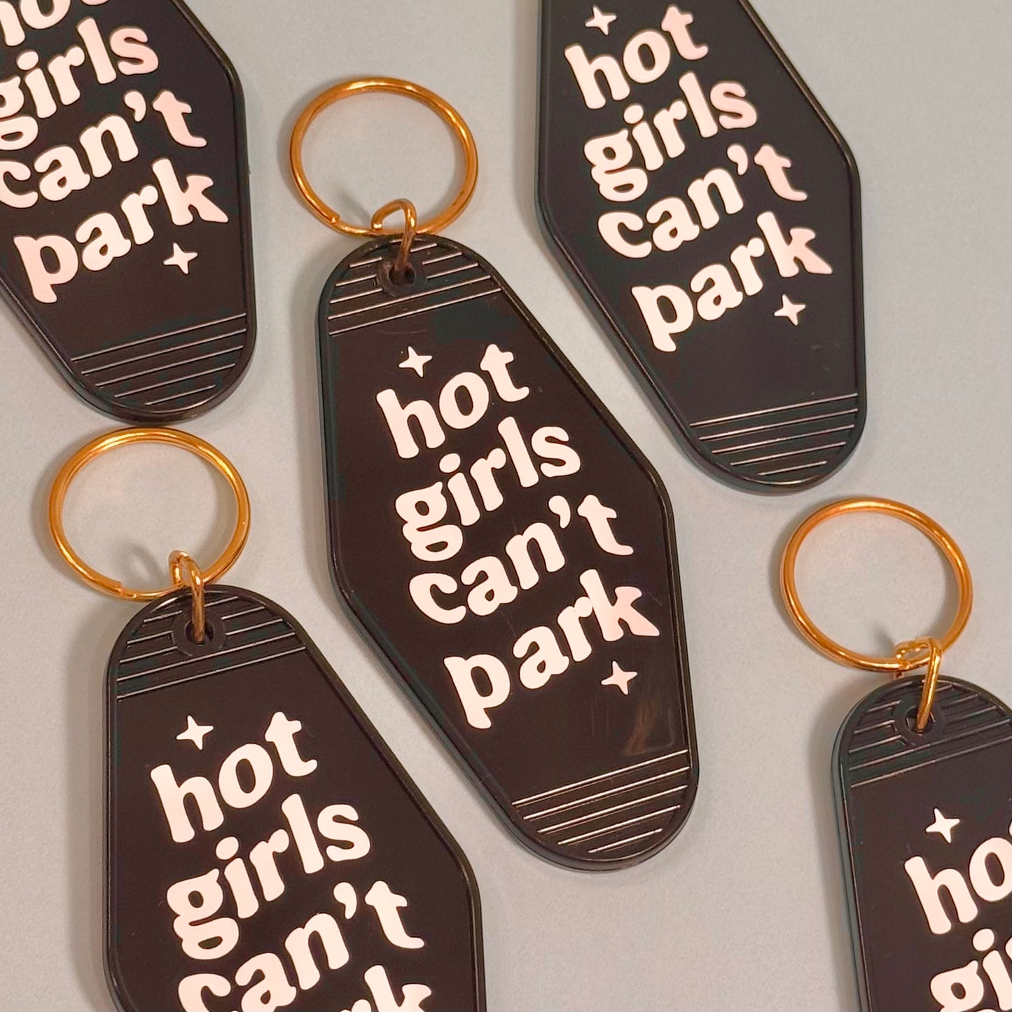 Keychains with 'hot girls can't park' text on a light gray background