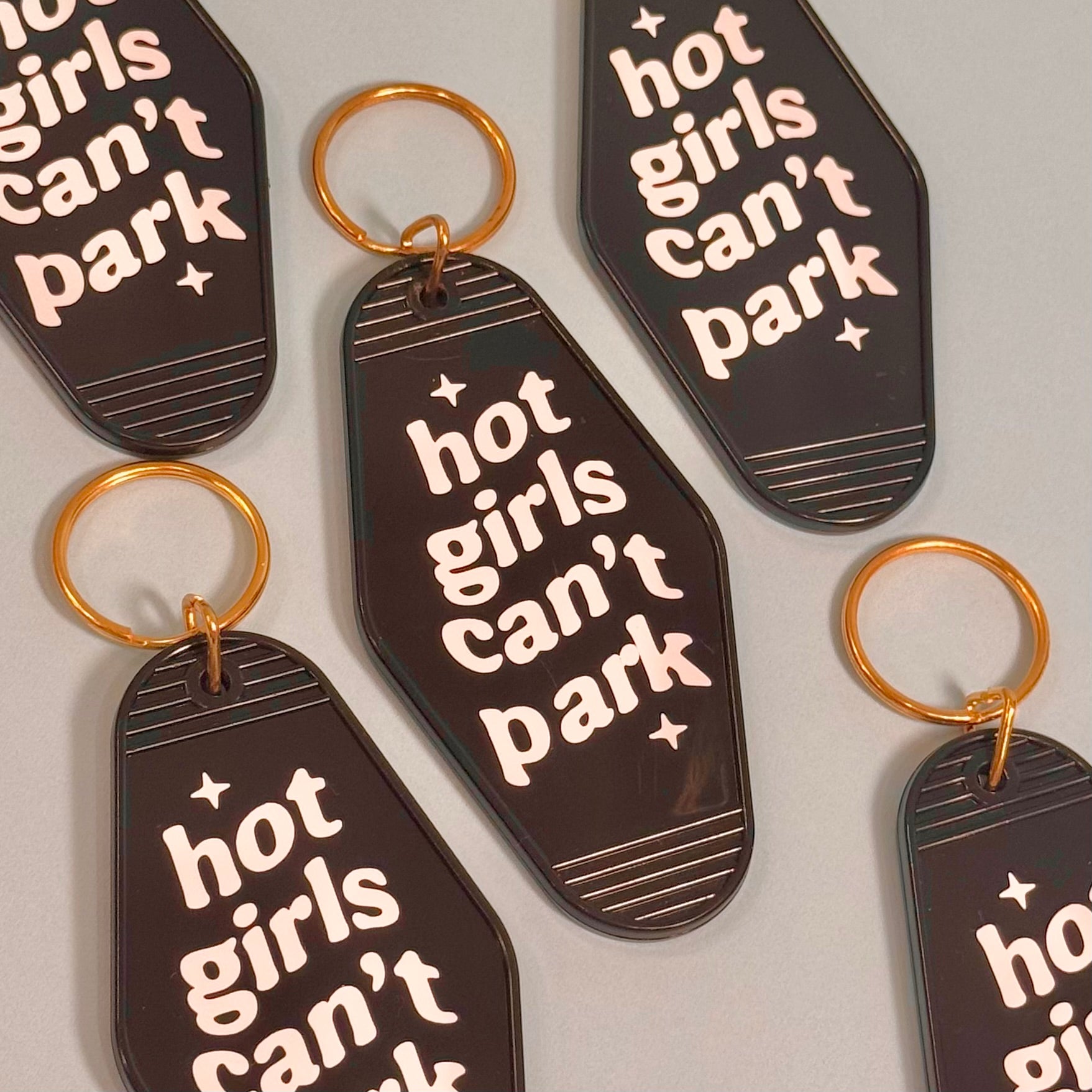 Keychains with 'hot girls can't park' text on a light gray background