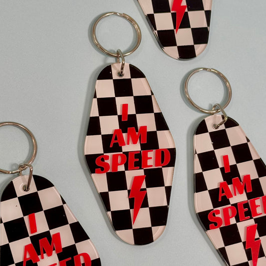 Black and white check board motel style keychain with red lettering “I am speed” and lightning bolt