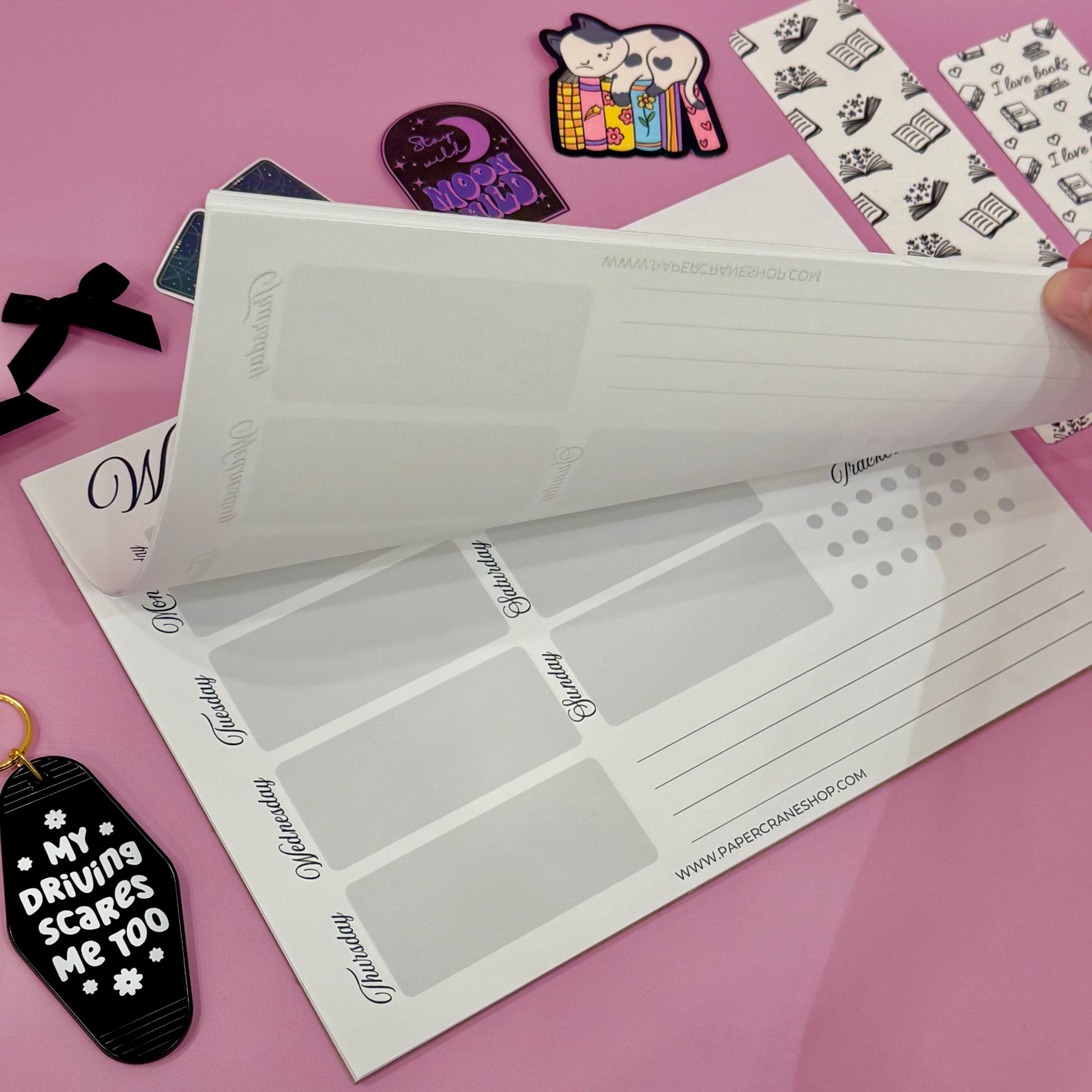 Black and White planner with text on a pink surface with decorative items.