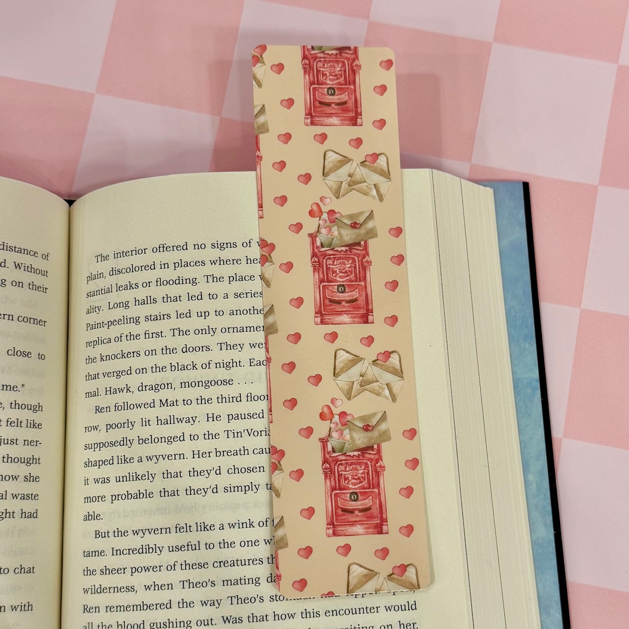 Decorative bookmark with heart and bow design on an open book against a pink checkered background