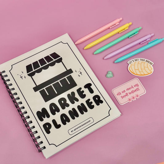 Notebook titled 'Market Planner' with colorful pens and stickers on a pink background