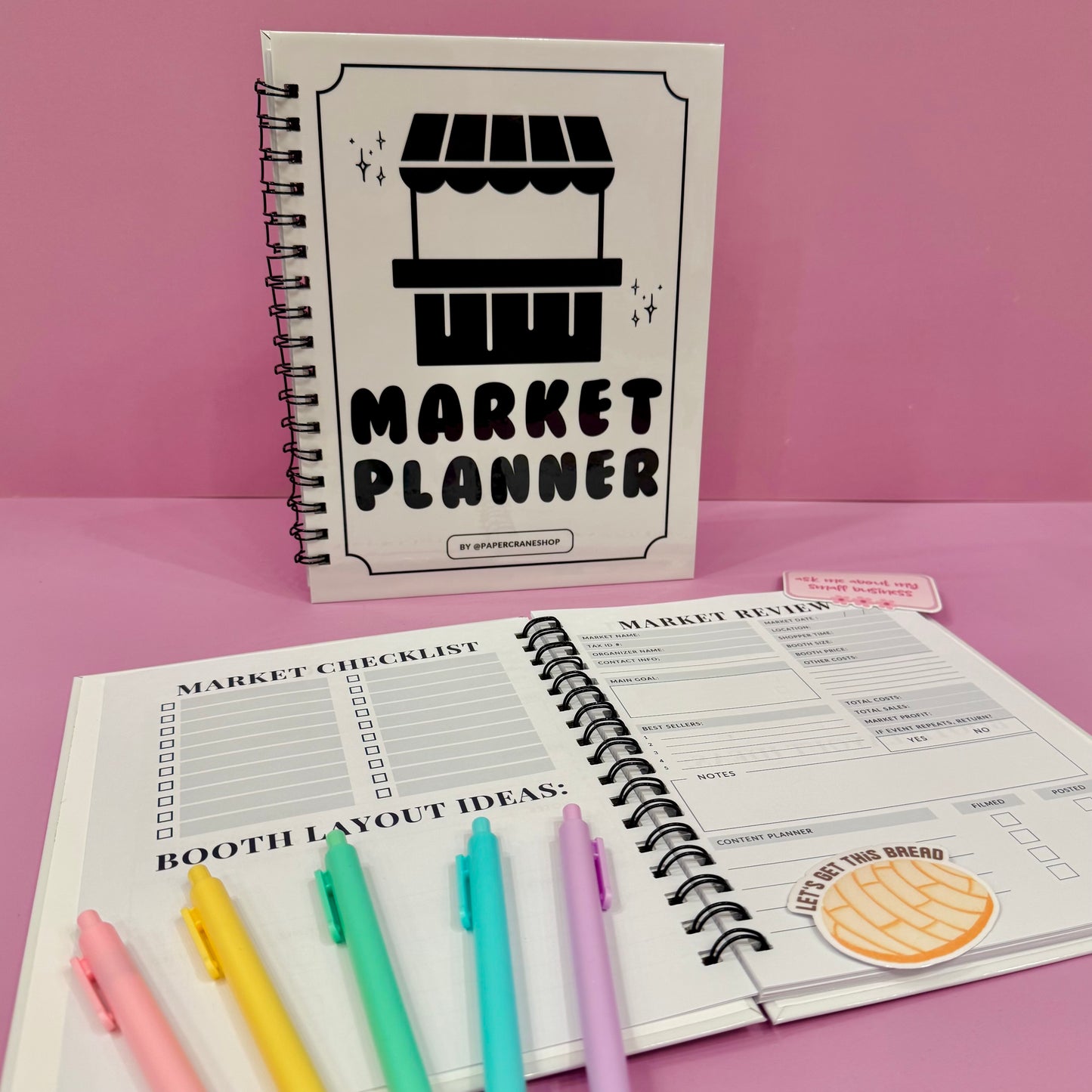 Market Planner notebook with colorful pens on a pink background