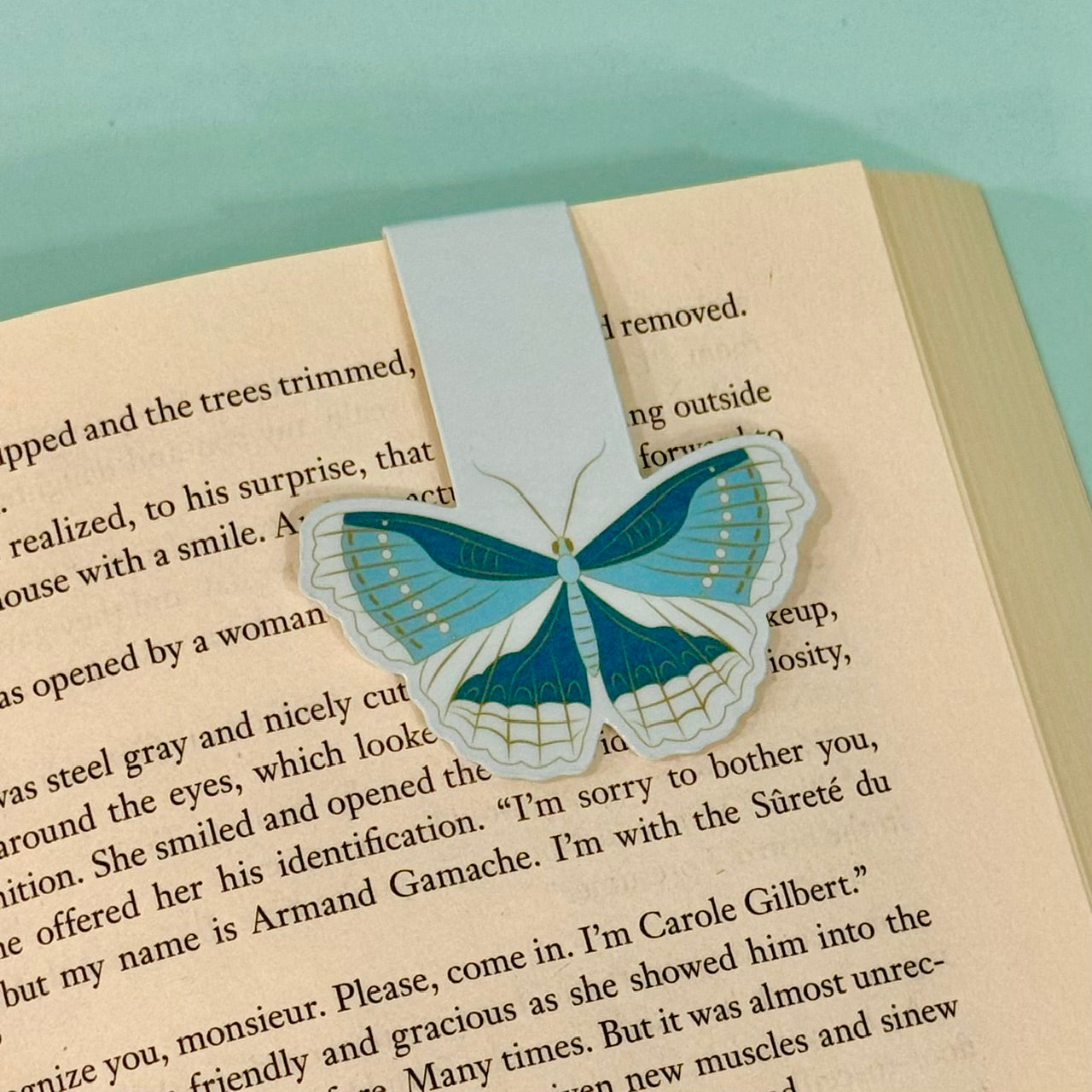 Moth-shaped blue magnetic bookmark on a book page with a light blue background