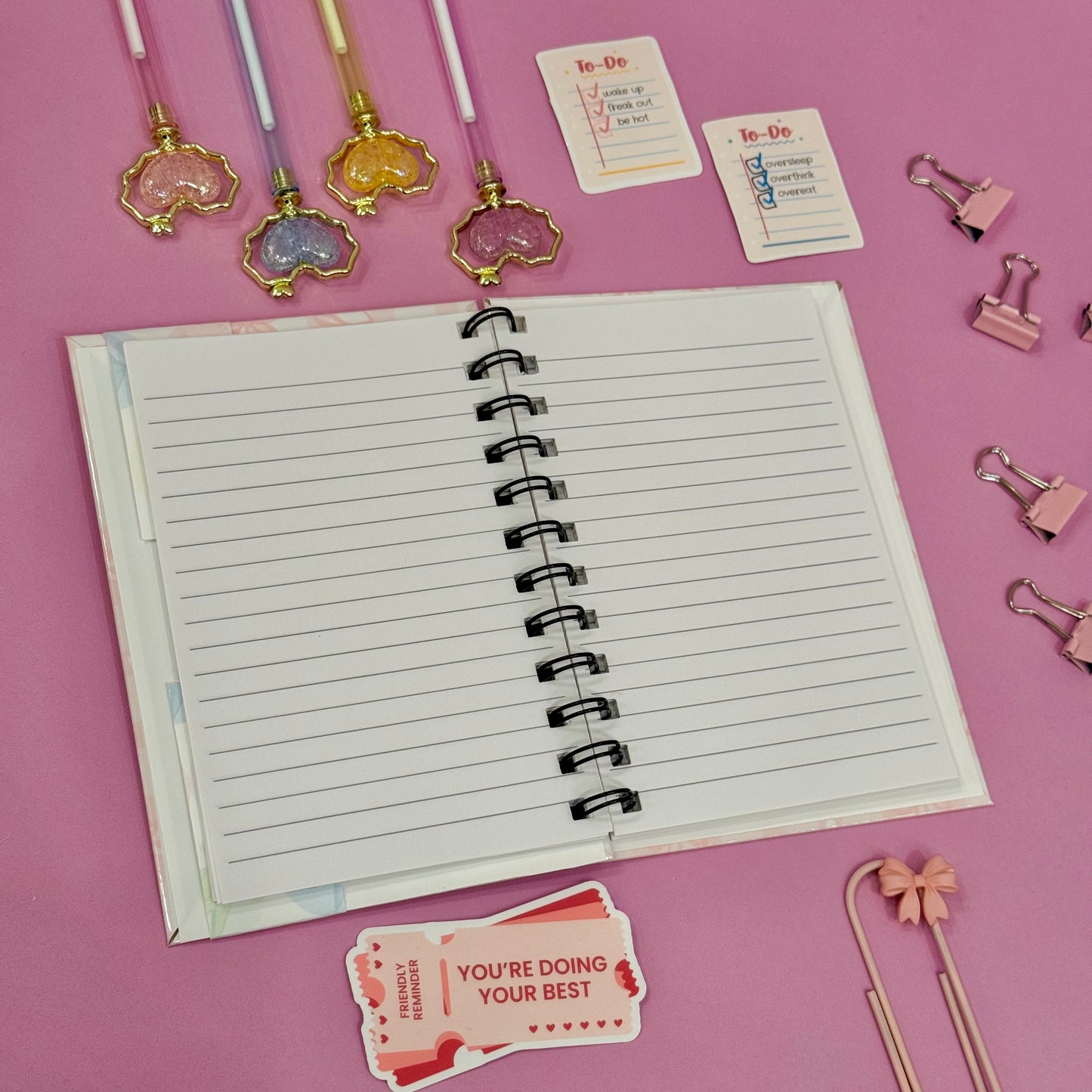 Open notebook with stationery items on a pink background
