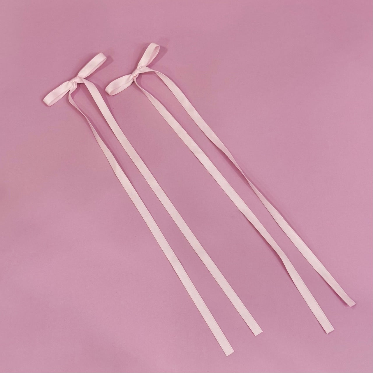 Two pink ribbons with bows on a pink background