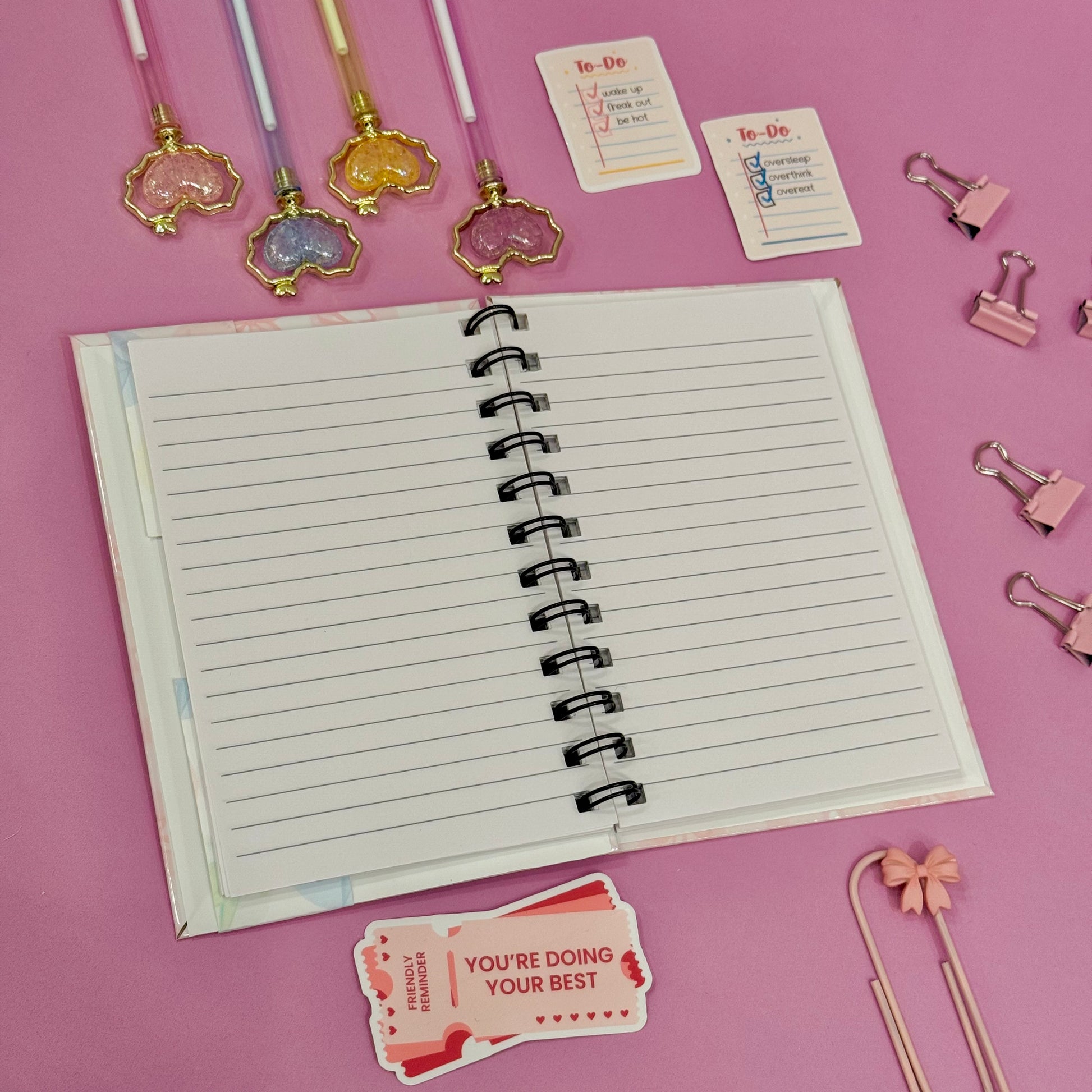 Open notebook with stationery items on a pink background