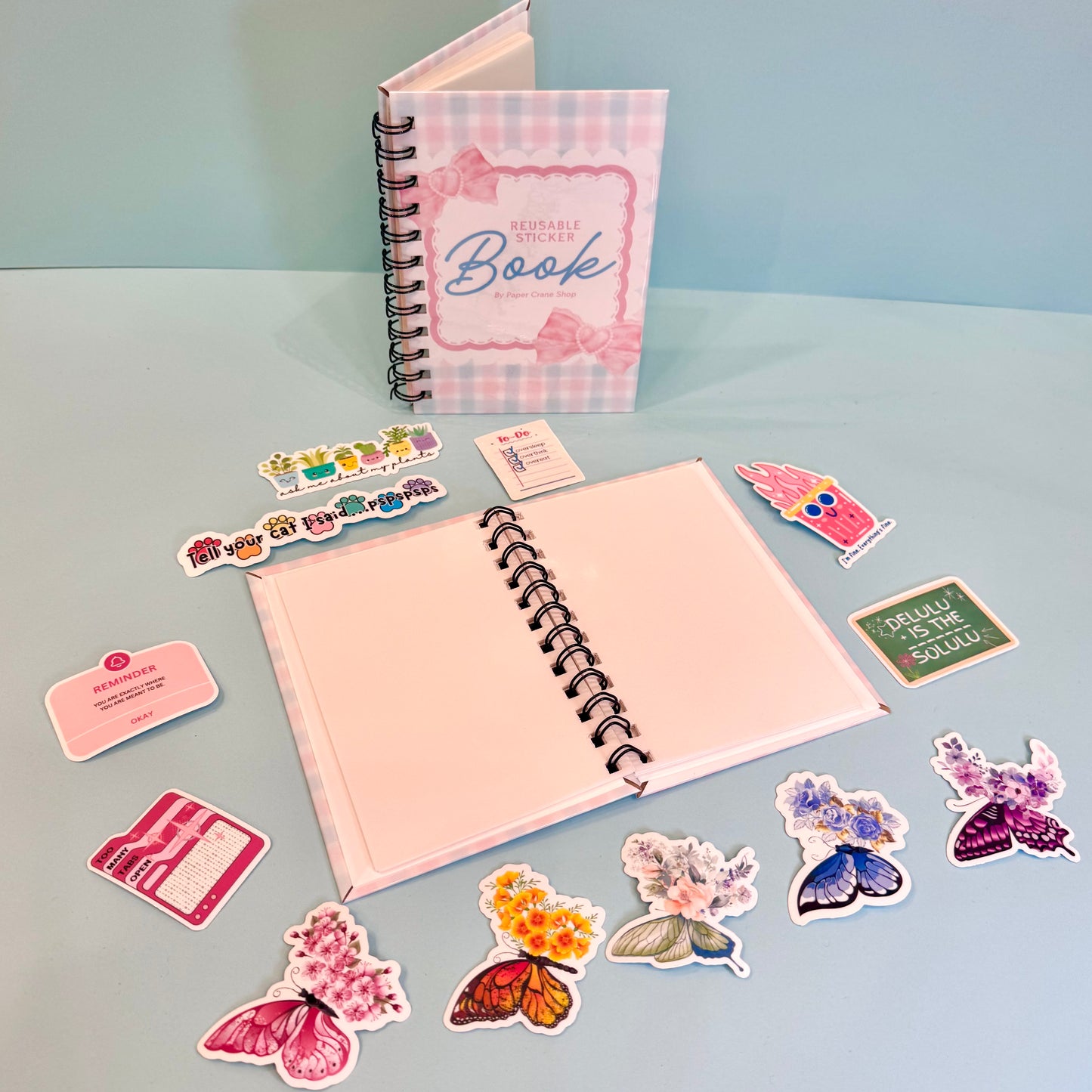 Open notebook with spiral binding, surrounded by various stickers on a light blue background