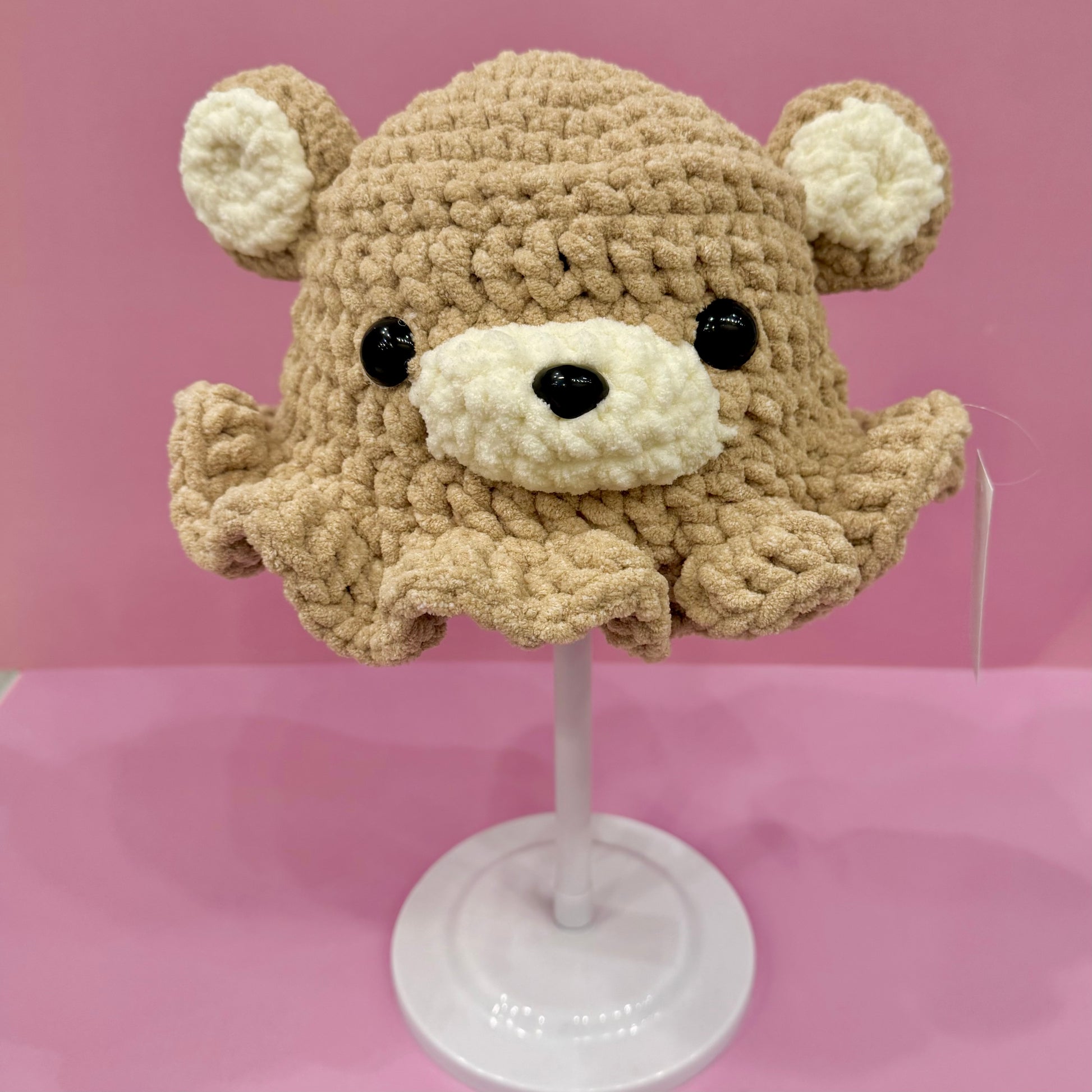 Crocheted bear hat on a mannequin head against a pink background
