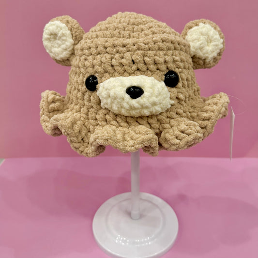 Crocheted bear hat on a mannequin head against a pink background
