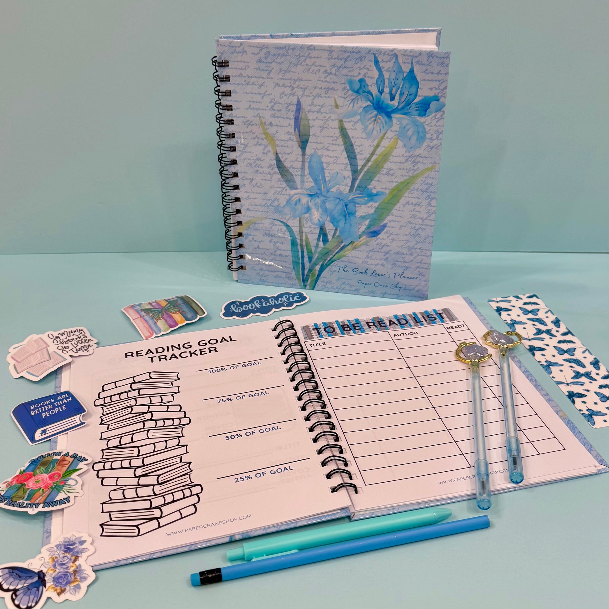 Notebook with floral design, reading goal tracker, and stationery items on a light blue background