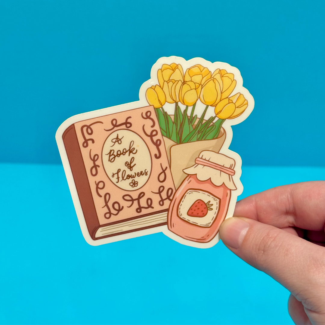 Sticker of a book titled 'A Book of Flowers' with yellow tulips and a jar of strawberry jam, held against a blue background.