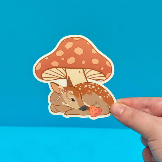 Sticker of a deer under a mushroom held by a hand against a blue background
