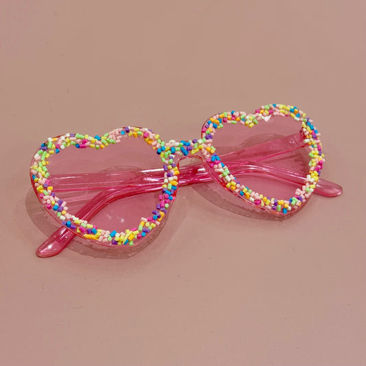 Colorful beaded sunglasses with pink frame on a beige background